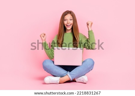 Full length photo of impressed lucky schoolgirl wear green sweatshirt rising fists reading modern gadget isolated pink color background
