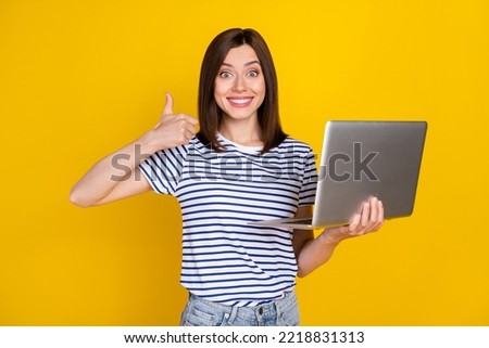 Photo of stunning young girl hold buy new laptop thumb up good quality wear stylish striped clothes isolated on yellow color background