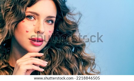 Beautiful model with drawn hearts on her cheeks posing in the studio. Fashion model is photographed in a photo studio looking at camera. Beautiful young woman with long hair.