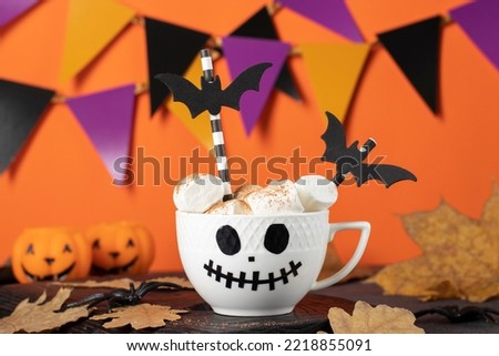 Chocolate drink for children with marshmallows and spices in white cup with scary Jack face. Home decorations DIY of colored paper