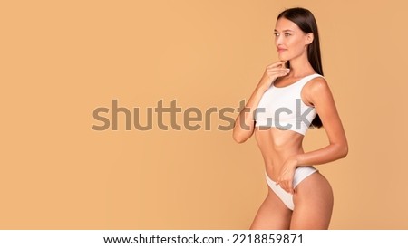 Beautiful slim lady in white underwear posing isolated on beige studio background, panorama with free space. Young woman with fit sporty slender body looking aside at copy space