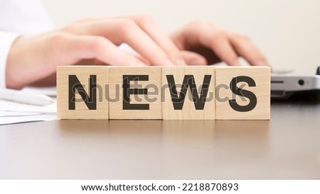 word NEWS made with wood blocks on the background man working of the laptop. selective focus.