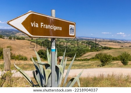 Landscape along via Francigena with Mud road, fields, trees and vineyard.  Sign showing the direction of Monteroni d'Arbia, route of the via francigena. Siena province, Tuscany. Italy, Europe.