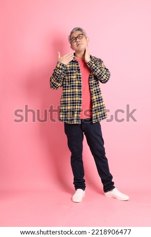 The full length of senior Asian man standing on the pink background.