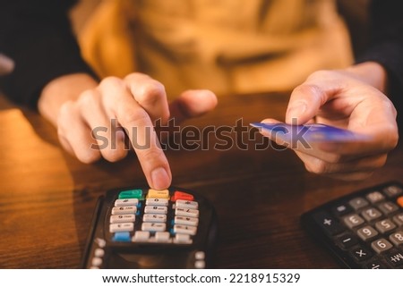Closeup of young Asian barista wearing an orange apron uniform filling bank debit and credit card detail on computer for payment from customer in modern cafe on ordering coffee and preparing bill