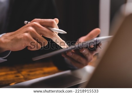 Closeup of hands of a successful business man and entrepreneur in formal clothing sitting in modern lighted office while holding pen and using digital tablet and reading document and making edits