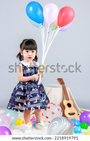 Portrait full body studio shot of little cute innocence kindergarten preschooler girl daughter in casual long blue dress standing smiling look at camera holding colorful balloons on gray background.