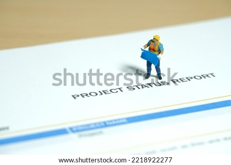 Miniature people toy figure photography. Project status report concept. A construction worker holding blueprint standing above progress report file on desk. Image photo