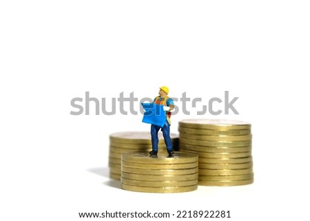 Miniature people toy figure photography. Project budget concept. A construction worker with blueprint building standing above golden coin money pile. Isolated on white background. Image photo