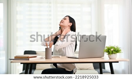Overworked young Asian businesswoman or female office worker suffering from neck pain after had a long day at work, massaging her neck. office syndrome concept Royalty-Free Stock Photo #2218925033