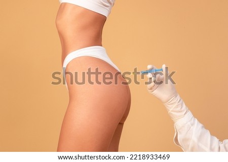 Non-sugical butt lifting sculptra concept. Side view of young woman getting hip injection at buttocks area, isolated on beige studio background, cropped Royalty-Free Stock Photo #2218933469