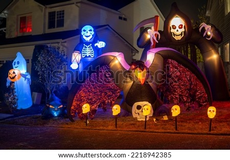 Night Halloween house outdoor decorations with glowing inflatable ghost, crow, skeleton, death, sculls with blue and orange lights