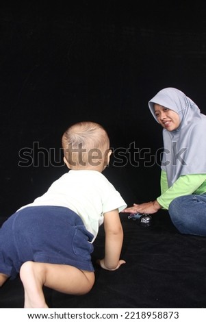 A baby crawls towards his mother on a black background
