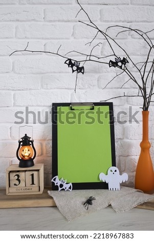 Vertical composition for the celebration of Helloween. A calendar, a flashlight, a ghost, a spider, bats, a vase with branches are on the table. A place for your text against a white brick wall. High