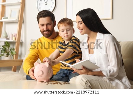 Happy family with notebook putting coin into piggy bank at home