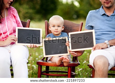 Happy family with little boy sitting on chairs and holding little blackboards in the meadow