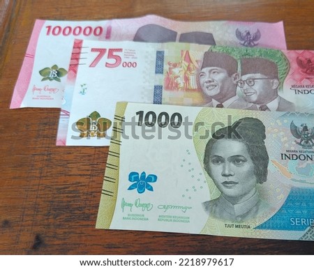The latest edition of Indonesian rupiah notes worth 1,000, 75,000 and 1.000, 75.000 dan 100,000 on a wooden background
