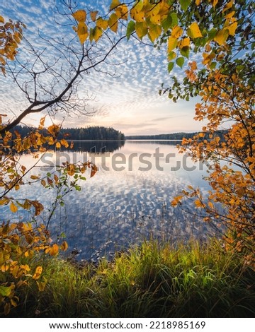 Autumn evening at the lake with beautiful cloud pattern and reflections in water. Trees framing the scene.