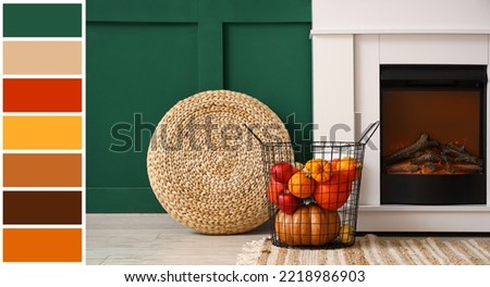 Modern fireplace, basket with pumpkins and wicker pouf near green wall. Different color patterns