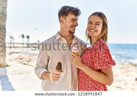 Young hispanic couple on vacation smiling happy eating ice cream at the beach