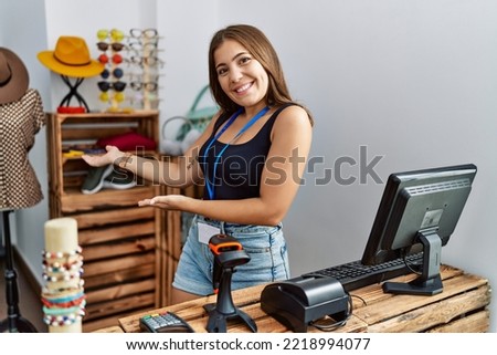 Young brunette woman holding banner with open text at retail shop inviting to enter smiling natural with open hand 