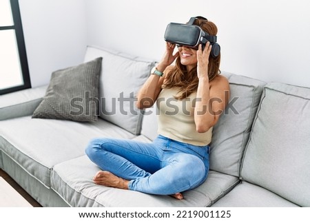 Young latin woman playing video game using virtual reality glasses at home