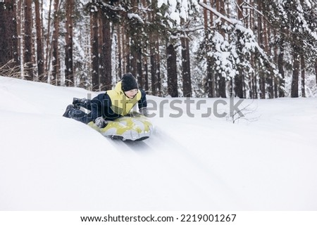 Joyful child boy sledding and having fun. Happy teenager riding on snow tubing in winter forest. Winter activity outdoors.