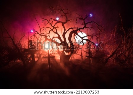 Spooky dark landscape showing silhouettes of trees in the swamp on misty night. Night mysterious forest in fire and dramatic cloudy night sky