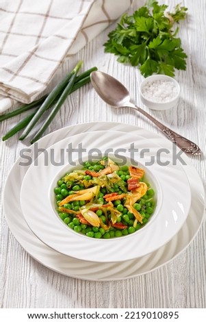 petits pois, french dish of tender, new-season peas braised in chicken stock with lettuce, onion bulbs and speck, cut into lardons, served in white bowl, vertical view