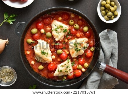 Cod stew with chickpeas, cherry tomatoes and olives in skillet over dark stone background. Top view, flat lay