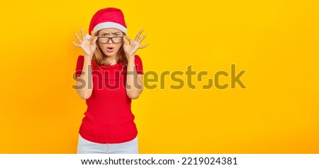 Surprised young Asian woman wearing Christmas hat with glasses while open mouth on yellow background