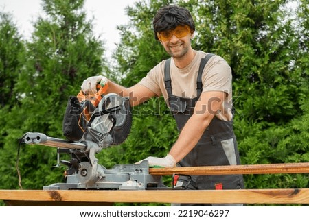 Professional carpenter works with a circular saw in the backyard. Royalty-Free Stock Photo #2219046297