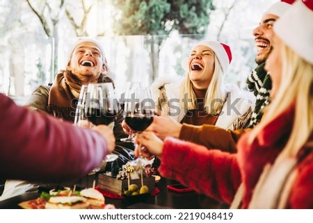 Happy family wearing santa claus hat having Christmas dinner party- Cheerful group of friends sitting at restaurant dining table celebrate xmas holiday cheering red wine glasses together Royalty-Free Stock Photo #2219048419
