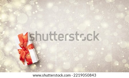 Minimalistic composition with a gift box with a wrapped red ribbon on a light stone background, close-up, top view. Holiday and congratulations concept
