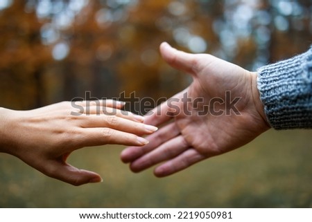 Young couple in love walking in autumn park holding hands close-up. The hands of a man and a woman reach each other.