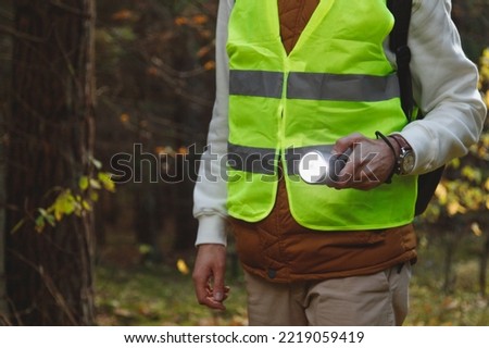 Male Volunteer of the Search and Rescue Team Dressed in a Signal Vest with a Flashlight in the Forest. Alone Man Lost in the Forest shines a Flashlight.