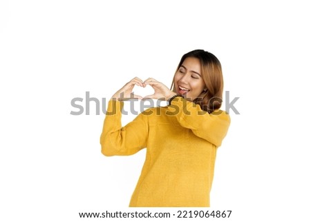 Attractive positive young asian brunette woman in yellow sweater on white background. showing love sign, heart shape for valentine day