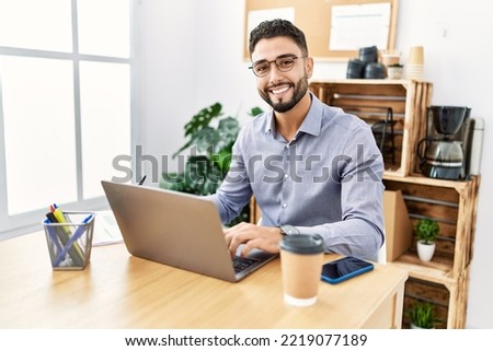 Young arab man smiling confident using laptop and writing on clipboard at office