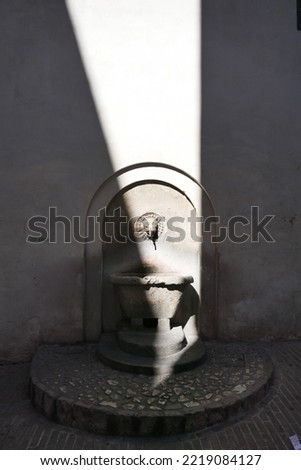 old stone wall fountain in narrow street in Spoleto with incident sunlight
