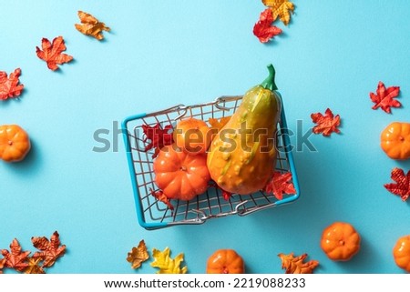 Autumn shopping design concept with shopping cart, maple leaves and pumpkin on blue table background.