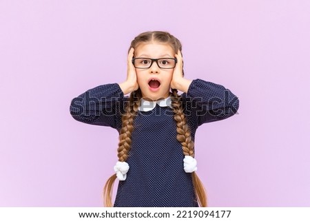 A very surprised little girl is holding her head with her hands, against an isolated background.
