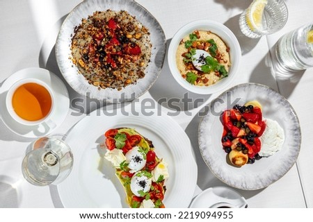 Italian breakfast. There are four morning meals on a table with a white tablecloth. Cheesecakes with berries, oatmeal with berries, oatmeal with nuts and poached egg, bruschetta with avocado, tomato a
