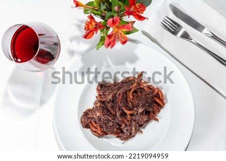 Italian dish. Pasta Bucatini with finely chopped duck fillet in plum sauce. The pasta lies in a deep, round, wide-brimmed ceramic plate. The plate is on the table on a white tablecloth. Next to the pl