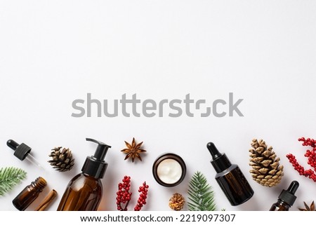 Natural cosmetics concept. Top view photo of amber glass pump bottle cream jar dropper bottle mistletoe berries spruce branches pine cones and anise on isolated white background with copyspace