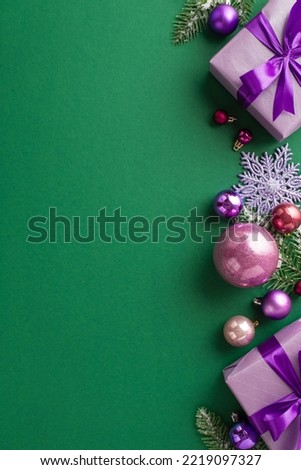 Christmas Eve concept. Top view vertical photo of lilac gift boxes with bows violet and pink baubles fir branches in hoarfrost and snowflake ornament on isolated green background with empty space