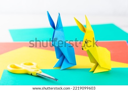Two multi-colored paper figures of origami bunnies on a table. Origami rabbit figures made of colored paper.