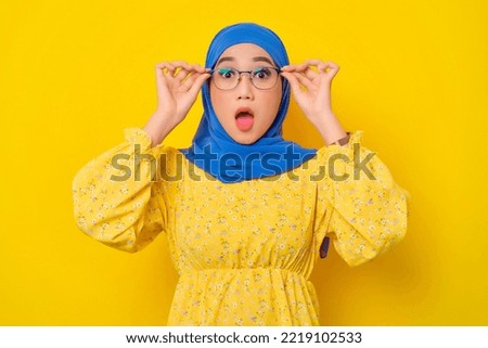 Surprised young beautiful Asian Muslim woman touching glasses with open mouth isolated over yellow background