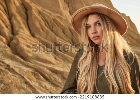 portrait of a beautiful young woman with long blond hair in a hat on a background of high beautiful sandy rocks and blue sky. beautiful sandy landscape