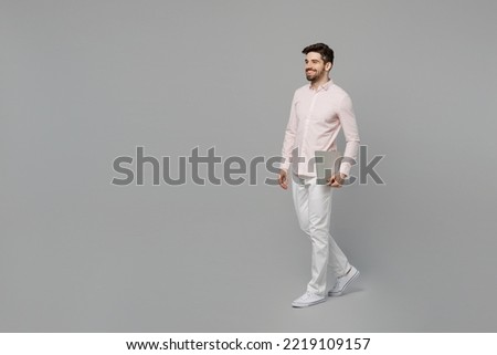 Full body young smiling cheerful happy fun cool caucasian IT man 20s he wearing basic shirt hold laptop pc computer isolated on plain grey color background studio portrait. People lifestyle concept