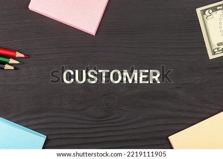 CUSTOMER - text, money dollars, stickers and colored pencils on a black wooden table. Business concept: buying, selling, commerce (copy space).